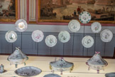 <center>Assiettes à huit accolades</center>Moustiers, fabrique Fouque (?)
Fin du XVIIIe siècle
Faïence stannifère, décor de petit feu en camaïeu vert
Marseille, Château Borély - Musée des Arts décoratifs, de la Faïence et de la Mode, inv. GF 3506
Avec le petit feu, Moustiers a satisfait au goût de l’exotisme, très prégnant dès le XVIIe siècle. Comme chez la Veuve Perrin (dont des productions sont présentées sur la table), le thème des chinoiseries est largement utilisé à Moustiers. Elles sont directement inspirées - mais non copiées pour autant - des gravures de Jean Pillement (1 728-1808), ornemaniste à l’origine de compositions rocailles où la figure du « Chinois » occupe une place centrale. Si la plupart des décors sont peints dans une polychromie associant du bleu, du jaune, du vert et du pourpre de Cassius, une particularité de Moustiers est d’avoir produit des « Chinois » en camaïeu vert, ce qui n’a pas été réalisé à Marseille.