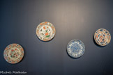 <center></center>De gauche à droite. Assiette
Chine, Jiangxi, Jingdezhen. Dynastie Qing (1644-1911), époque Qianlong (r. 1736-1795)
Porcelaine, émaux de la famille rose. Au XVIIIe siècle, la porcelaine chinoise se pare de couleurs plus nuancées. Le pigment composé de chlorure d’or n’est introduit qu’en 1728 dans les fours de Jingdezhen, permettant alors l’éclosion de la famille rose.
Le rose, employé en camaïeu, s’associe ici à des couleurs plus criardes, telles que le jaune, le vert et le turquoise, qui le rapprochent d’une esthétique postérieure.
Sous Qianlong, les exportations de pièces polychromes vont croissantes. Le décor dit « aux cent antiques » ou « à l’échantillon » correspond au goût des Occidentaux pour l’exotisme.
<br>
Assiette
Chine.
Dynastie Qing (1644-1911), époque Kangxi (r. 1661-1722)
Marque, au revers : les deux cercles, en bleu sous couverte. Porcelaine, émaux de la famille verte. Le bassin de cette assiette aux émaux sur couverte de la famille verte, cerné par un filet noir, est orné du motif conventionnel « fleurs et oiseaux » huaniao, hérité des peintures académiques des Song du Nord (900-1126).
La palette caractéristique de la famille verte est appelée en Chine « couleurs vives », yingcai. Cette production atteint sa pleine expression sous le règne de Kangxi, qui se réapproprie les couleurs déjà utilisées sous les Ming (1368-1644), en les associant à du rouge de fer et d’autres nuances de vert
<br> Plat creux.
Chine
Dynastie Qing (1644-1911), époque Kangxi (r. 1654-1722)<br>Assiette
Chine.
Dynastie Qing (1644-1911).
<br>Legs Magdeleine Dauphin (collection Jean- Baptiste Dauphin), 1918. Fonds Musée des Beaux-Arts
Marseille, Château Borély - Musée des Arts décoratifs, de la Faïence et de la Mode.