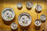 <center>Décor dit au chrysanthème.</center>Connu en Europe dès le XVIIe siècle par des gravures, le chrysanthème, ou « fleur d'or», est importé pour la première fois en France par te Marseillais Pierre Blancard en 1788. Symbole de longévité en Chine, allégorie du pouvoir impérial au Japon, il a été à l'origine d'un décor largement diffusé par la Compagnie des Indes qui semble avoir retenu l'attention de faïenciers provençaux.
Ainsi, cet ensemble d'assiettes et de plats peut être attribué l'atelier de la Veuve Perrin grâce à la présence caractéristique d'insectes, tant sur les grands plats que sur les assiettes de grand feu et petit feu, mais aussi à la figuration de tiges parallèles pour divers bouquets en camaïeu et en polychromie. S'il est admis que ce décor puise son inspiration d’un modèle sur porcelaine de la Compagnie des Indes de l’époque Qianlong, on sait aussi que certains décors ont été à leur tour largement copiés dans des ateliers asiatiques afin de satisfaire des commandes européennes pléthoriques.<br> Assiettes et plats à décor dit au chrysanthème Marseille, attribués à la fabrique Veuve Perrin Fin XVIIIe siècle
Faïence stannifère, décor de petit feu polychrome, sauf celle en haut, à droite (fleurs rose) : Chine, Compagnie des Indes.
Epoque Qianlong (r. 1735-1796), entre 1760 et 1780 Porcelaine, émaux de la famille rose et or.
Collection particulière.