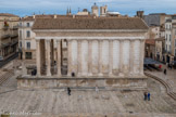 <center>La Maison Carrée.</center>Cet édifice a été bâti entre 10 av. J.-C. et 4 apr. J.-C., à l’extrémité sud du forum, sous le règne d’Auguste.
La place du forum où a été édifié le temple s’étendait sur 80 m de long et était encadrée par un double portique sur les côtés est et ouest. Au sud, la place était fermée par un mur aveugle orné de pilastres et au nord, par un bâtiment rectangulaire de 18 par 14 m, que l’on identifie aujourd’hui comme étant la curie. Le temple s'inscrivait ainsi dans un péribole délimité par cette place.