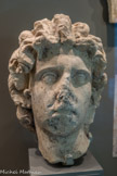 <center></center>Portrait masculin, Alexandre (?). Les traits virils, l’anatomie charpentée et la coiffure léonine de ce portrait rappellent les représentations d’Alexandre. Les mèches frontales relevées, appelées anastola 'sont caractéristiques. Le regard levé et le mouvement vif expriment la force de son caractère et la fulgurance de son destin. Cette œuvre a pour modèle le type d’Alexandre Boston-Capitole dont, l’original est daté des années 150-100 av. J. C. Il présente une forte idéalisation des traits et un rapprochement formel avec les représentations d’Hélios liés à une volonté d’assimilation entre le dieu solaire et le personnage. Cette assimilation apporte une aura divine à Alexandre. Fin Ier s. - première moitié du IIe s. ap. J.-C. Marbre blanc