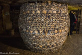 <center>Les Catacombes de Paris. </center> Une vaste salle entièrement ceinte d'ossements, dite « crypte de la Passion » ou « rotonde des tibias », est dotée d'une étrange sculpture d'ossements, en forme de tonneau. Celui-ci est exclusivement constitué de tibias, autour d'un pilier de consolidation. C'est dans cette salle que se déroule le concert clandestin du 2 avril 1897.