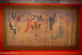 <center>Paul Poiret, la mode est une fête</center>Raoul Dufy
Tenture, La Présentation des mannequins chez Poiret
Livrée par l'artiste à Paul Poiret pour la péniche Orgues
1925
Toile de coton imprimée et peinte en couleurs rongeantes. Centre Pompidou, Paris
Musée national d'art moderne - Centre de création industrielle, achat, 1937
En dépôt au musée des Arts décoratifs de Paris depuis 1985
Raoul Dufy Bianchini Ferier
Cette tenture illustrant un défilé de modèles Poiret est la huitième d’un ensemble de quatorze toiles exécutées par Raoul Dufy, destinées à habiller les murs de la péniche Orgues, où a lieu chaque après-midi une présentation des créations de la maison de couture. Réalisée dans son atelier de Tournon avec le concours technique de la maison lyonnaise Bianchini Férier, elle est composée de trois lés assemblés et d’une bordure imprimée dans lesquels évoluent les personnages sans notion d’échelle. L’artiste applique ici sur des motifs préalablement dessinés le procédé des couleurs dites « rongeantes», qui s’incrustent dans la toile en se substituant à la teinte d’origine.