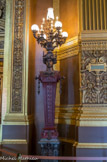 <center>Le grand foyer. </center> Quatre têtes de femmes modelées par Chabaud soutiennent les lampes qui représentent les différents modes d'éclairage : huile, bougie, gaz et électricité.