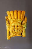 <center>CULTES ET RELIGIONS</center>Chaque cité grecque honore ses dieux : Zeus, Aphrodite, Déméter... Les cultes d’Alexandre, des Ptolémées, de Dionysos et Sérapis ont une importance particulière. Les Grecs ont établi des similitudes entre leurs dieux et ceux adorés par les Égyptiens. Alexandrie compte plusieurs synagogues. <br>
Fragment d’amulette figurant le dieu égyptien Bès.
Basse Époque, 943-716 av. J.-C.
Égypte, faïence égyptienne
Paris, musée du Louvre, département des Antiquités égyptiennes