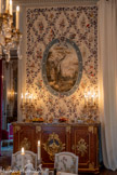 <center>La Salle à manger </center>Buffet.  Jean-Henri Riesener. 1785. bois de violette ; marbre ; bronze : doré. Buffet à trois portes avec placage de bois de violette, marbre Rance et bronze doré. La façade est tripartite, à ressaut plat central. Elle est liée aux côtés rectangulaires par des pans coupés droits sur plan curviligne. Le dessus de marbre épouse la découpe générale. Chaque méplat central est délimité par une moulure, et le centre des panneaux est occupé par deux chutes de trophées pour les côtés, représentant les attributs des Sciences et des Arts et, sur le vantail central, de la figure d'Uranie ou Minerve dans un ovale accosté de palmes, ces trois motifs étant suspendus par un noeud de ruban. Le meuble compte deux entrées de serrure dans un goût rocaille.