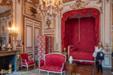 <center>Chambre sur cour.</center>Lit de travers. Le lit de travers est un type de lit qui se plaçait parallèlement au mur, ce qui suppose qu'un des longs côtés est moins décoré que l'autre, n'étant pas visible. Lit composé de deux chevets égaux garnis, reposant sur quatre pieds tournés en culot de feuilles d'acanthe. Les dés de raccordement carrés sont ornés de rosaces et surmontés par les montants antérieurs tournés en carquois sculpté, à écailles. Ils sont prolongés par deux bagues perlées sous rais de coeur, un dé à rosace et un sommet en plumes de flèches. Les montants postérieurs sont carrés et cannelés à chandelles. Les bâtis intérieurs sont moulurés, et les traverses supérieures en anse de panier ont des extrémités droites et des arêtes supérieures en ruban torsadé. Le pan de façade est mouluré à tablier, sculpté et ajouré. Il porte en sa partie centrale un cercle à deux coeurs transpercés de deux flèches, sur une branche à petites feuilles prolongées en ruban torsadé.