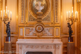 <center>Salon d'honneur.</center>Paire de candélabres représentant un satyre portant une corne d'abondance ornée d'un décor de stries de laquelle sortent des fleurs et sept bras de lumière en bronze ciselé et doré. Au centre du bouquet s'échappe un huitième bras de lumière en forme de tulipe. Le satyre nu, en bronze patiné, est en équilibre sur une seule jambe accolée à un tronc d'arbre. La jambe portante repose sur un socle de marbre griotte en forme de fût de colonne cannelé.<br> Pendule constituée d'un simple cadran circulaire encastré dans le décor de la cheminée du salon d'honneur. Le cadran est incisé de motifs de rinceaux et d'une tête d'Apollon en son centre. Il est percé de douze ouvertures laissant voir les chiffres romains de la plaque émaillée sous-jacente. 1850-1899.