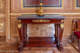 <center>Galerie des ports de guerre </center>Paire de consoles en placage d'acajou et acajou flammé ouvrant par un tiroir en ceinture et comportant un fond de glace ancien, dessus de marbre gris Sainte-Anne. La ceinture, est marquée au centre par une rosace à bouton flaquée de fleurons et palmettes, les angles sont timbrés de fleurette. Les pieds en pattes de lion sont ornés de palmettes en bronze doré. Ils reposent sur une plinthe formant une tablette d’entretoise. 1800-1824. Pierre Antoine Bellangé (1760-1844), reçu maître menuisier le 24 octobre 1788. Il s’installe dans un atelier de la rue Neuve Saint-Denis (actuel rue Blondel à Paris). Avec la Révolution et la libéralisation des métiers engendrée par la loi d’Allarde (2 mars 1791) et la loi Le Chapelier (14 juin 1791) qui mettent fin au régime des corporations, Bellangé peut élargir son activité à l’ébénisterie. Dès l’époque consulaire, le maître occupe une place importante parmi les fabricants de luxe parisiens. Il obtient un brevet de fournisseur officiel du Garde-Meuble impérial en 1811. Il jouit de la même faveur sous la Restauration et Louis-Philippe le nomme « ébéniste du roi » sous la Monarchie de Juillet.