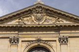 <center>Notre-Dame-des-Victoires. </center>Le portail est couronné par un fronton triangulaire avec au tympan, un écusson aux armes de la France surmonté de la couronne royale et entouré du grand cordon du Saint-Esprit. Pilastres d'ordre corinthien.