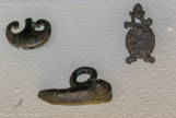 <center>25. Plot de calage. Métal. Plot de calage de vase en forme de pelle.
26. Pendentif. Alliage cuivreux. Epoque romaine. Ex-voto en forme de phallus.
27. Applique. Métal. </venter>