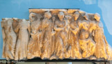 <center> Sarcophage des Muses. </center> Marbre blanc. Provient d'Arles. IIe siècle. Ce décor de sarcophage, malheureusenient dégradé, était déjà exposé avant la Révolution dans le musée installé par les Minimes à Saint-Honoras-des Alyscamps. Apollon, dieu de la musique et de la poésie, y est figuré entouré des Muses dont il préside les jeux sur le Mont Parnasse.
Il est au centre de la composition, reconnaissable à la lyre qu'il tient dans la main droite ramenée contre la poitrine et au corbeau, oiseau qui lui était consacré, situé à ses pieds: De part et d'autre du dieu sont- réparties les Muses, filles de Zeus et de Mnémosyne, personnification de la mémoire. Ces neuf soeurs qui représentent la pensée sous toutes ses formes, chantent, égaient lors des fêtes organisées par les dieux. Ici, seules sont reconnaissables à gauche d'Apollon, Mélpomène (laTragédie), portante une massue, et Thalie (la comédie) tenant un masque de théâtre.