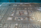 <center>Mosaïque</center>L'opus tessellatum est un tecnique qui utilise des tesselles (petits cubes de pierre taillés, d'environ 1 cm de côté). L'un d'eux ornait le triclinium (salle à manger) d'une des maisons. Son décor représente le dieu Aiôn tenant la roue du zodiaque encadré de Néréides, d'animaux marins et des quatre saisons.