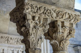 <center>Cloitre de St Trophime</center>galerie Nord. Chapiteau à trois rangs de feuilles d'acanthe, sans trace de trépan. Quatre têtes  (deux masques humains, et ici une tête de bélier et une tête de griffon) sortent de deux rangs de feuillage.