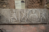 <center>Fragment sde couvercle de sarcophage.</center>IVe-Ve siècle, fragment de la frise (partie droite), marbre de Carrare.
De l'ancienne partie centrale, brisée, reste une partie de la tessère anépigraphe portée par un génie ailé se détournant. À droite, deux autres génies présentent l’imago clipeata de la défunte qui tient un volumen dans sa main droite.