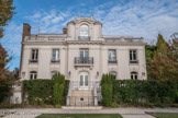 <center>Enghien-les-Bains. </center> La Villa du Lac. La façade donnant sur le lac est complètement à l’opposée : c’est celle d’une villa-château. L’enduit est blanc, et la façade est décorée avec des éléments de style classique. Elle est caractérisée par sa symétrie : de chaque côté de la partie centrale en saillie, deux travées sont composées de baies rectangulaires à l’étage et arrondies par des arcs en rez-de-chaussée. Un garde-corps entoure la terrasse en partie basse, et le même est rappelé au-dessus de l’étage.