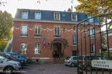<center>Enghien-les-Bains. </center> La Villa du Lac. L’opposition des deux façades est très marquée. Du côté rue, la façade en briques rouges est décorée par une guirlande en briques blanches. Le perron est surmonté d’une marquise semi-cylindrique. Cette façade « urbaine » est ajoutée à la construction originale : on « double » l’édifice en 1928 par ce corps de bâtiment en briques.