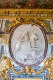 <center>Le salon de la Guerre. </center> Le triomphe de Louis XIV, le roi à cheval, en armure antique, foulant au pied ses ennemis et couronné par la Gloire, médaillon en stuc de Coysevox. Ce bas-relief est surmonté de deux Renommées dorées et soutenu par deux captifs enchaînés. Ce salon est situé au bout des Grands Appartements du Roi, et déjà il n'en fait plus partie. En effet, placé à l'angle nord-ouest du corps central, il forme avec la Galerie des Glaces et le Salon de la Paix un ensemble grandiose et majestueux qui occupe toute la façade du corps central.