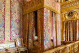 <center>La Chambre du Roi.</center> Cette chambre de parade fut réalisée sur l’emplacement du salon du roi, une pièce qui remontait à l’époque de Louis XIII. Lors du règne de Louis XIV, elle subit maintes modifications jusqu'à son achèvement en 1701 Avec l’établissement de la chambre du roi, la pièce devint le centre physique et idéologique du château : le souverain y dînait au « petit couvert ». Chaque jour avaient lieu les cérémonies du « lever » et du « coucher » du Roi, auxquels assistaient une centaine de personnes (officiers de la chambre et de la garde-robe, courtisans, diplomates, gouverneurs Le 1er septembre 1715, Louis XIV, âgé de 76 ans, y mourut. La ruelle (nom de l'alcôve attenante au lit) où se trouve le lit du roi, est séparée de l’autre partie de la pièce par une balustrade en bois doré séparant l'espace public de l'espace privé dans lequel seuls les domestiques et les membres de la famille royale pouvaient accéder. Les tentures de la ruelle et du lit sontt de velours cramoisi brodé d’or tendu sur les murs en hiver, damas d’or et d’argent sur fond de damas cramoisi en été. Le lit présenté dans la Grande chambre du Roi, à cet emplacement depuis 1701, est la restitution du meuble d’été en place de 1723 à 1785, commandé par Louis XV quand il retourna vivre au château. Au-dessus de la porte, Sainte Madeleine de Zampieri, Domenico dit le Dominiquin.