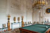 <center> Le Grand Trianon.</center> Le salon de Musique. C’est l’ancienne antichambre du premier appartement de Louis XIV, où avait lieu le souper du roi. Les boiseries comptent parmi les plus anciennes du palais, et l’on remarque, au-dessus des portes, les volets des tribunes où prenaient place les musiciens qui jouaient pendant le repas. Napoléon fit de cette pièce le salon des Officiers, et Louis-Philippe une salle de billard. Les chaises recouvertes de tapisserie de Beauvais ont été exécutées pour cette pièce. Les tableaux représentant Mars et Minerve (photo) proviennent de l’antichambre des Jeux et de la chambre du Sommeil. Sur la cheminée, la fontaine à thé.