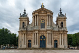<center> La cathédrale Saint-Louis.</center> C'est une église de style rocaille construite par l'architecte Jacques Hardouin-Mansart de Sagonne de 1743 à 1754. En 1790, Versailles devint siège d'un évêché. Le premier évêque constitutionnel, Monseigneur Avoine, choisit Notre-Dame pour cathédrale. Juchée sur un vaste perron de huit marches, la façade s'élève sur deux niveaux. L'étage inférieur comprend trois portes. La principale est flanquée de six colonnes doriques. Les deux portes latérales sont flanquées de deux colonnes du même ordre en forte saillie, qui portent des pots à feu à pieds en forme de console. Le second niveau occupe la partie centrale. Il s'orne de colonnes corinthiennes disposées comme à l'étage inférieur. Il se compose d'une baie en plein cintre qu'occupe une horloge. Cette ouverture est coiffée d'un linge inspiré de celui que Robert de Cotte, grand-oncle de l'architecte, réalisa pour la cathédrale de Montauban. Deux larges volutes inversées entourent le motif de façon originale.