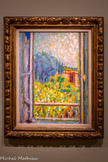 <center>LA PETITE FENÊTRE</center>1946
Huile sur toile
COLLECTION BELGE LGR
Après avoir acquis en 1912 un tableau de son ami Matisse représentant un paysage vu à travers une fenêtre ouverte. Bonnard se lance à son tour dans des compositions où la fenêtre, un élément géométrique et stable, sert de cadre à des vues foisonnantes. Il met ici en scène la vue qu'il contemple quotidiennement depuis la chambre à coucher de sa maison du Cannet. Le jardin, résumé à deux plans contrastés dominés par des jaunes et des bleutés, est traité de manière synthétique comme une expansion de couleurs en fusion, de lumière et d'ombre sous un ciel pommelé de petites touches de nuances nacrées.