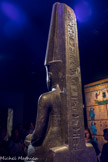 Amon protégeant Toutankhamon.
Diorite.
Règne de Toutankhamon 1336-1326 av. J.C. <br>
Dans le texte sur le pilier dorsal, les prêtres et les scribes du règne de Toutânkhamon, avaient manifesté pleinement le retour à l’orthodoxie voulue par l’entourage de l’enfant-pharaon. Cela n'a toutefois pas suffi, à le protéger d'Horemheb,  général d'armée qui monta plus tard sur le trône. À leur tour ses prêtres, scribes et graveurs eurent la charge d'effacer les noms du roi. Ils oublièrent deux minuscules cartouches, gravés sur le côté droit du pagne royal, laissant ainsi une chance supplémentaire à Toutânkhamon de traverser les siècles.gravés sur le côté droit du pagne royal, laissant ainsi une chance supplémentaire à Toutânkhamon de traverser les siècles.