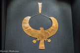 Collier ousekh en or avec contrepoids : faucon avec aux ailes déployées
Or.<br> Les embaumeurs plaçaient plusieurs colliers ousekh entre les couches de bandelettes de la momie. Ces colliers étaient aussi bien portés par les dieux que par les hommes et les femmes.
Le faucon représente Horus, le dieu intimement lié au pharaon vivant. À la fois fils d'Osiris et de Rê, Horus montait en flèche dans le ciel comme le faisait le faucon dans l'ancienne mythologie égyptienne, Les fils d’or enfilés dans les trous au bout des ailes retiennent un contrepoids en fleurs de lotus de forme allongée suspendu dans le dos du porteur, équilibrant le poids du pendentif