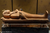 Figurine osirienne en bois de Toutânkhamon allongé sur une bière
Les différentes enveloppes funéraires et les bandelettes de la momie sculptée, ainsi que la tête et les pattes de lion du lit protègent le personnage contre les forces surnaturelles.
Bois, feuille d’or.