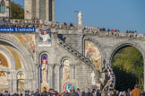 <center>Lourdes.</center>Basilique Notre-Dame-du-Rosaire. Vers l'extérieur, elle s'ouvre sur une vaste esplanade (dite « Esplanade du Rosaire ») pouvant rassembler quelques 80 000 visiteurs, encadrée par deux rampes d'accès en hémicycle supportées par des structures en arcades permettant de gagner la basilique de l'Immaculée Conception, située au-dessus. osaïque de droite : la Transfiguration. ; derrière les rampes, la guérison du paralytique. Les arcades supportent des statues datant des années 1910 à 1914, de bas en haut et symétriquement disposées : Saint Pierre et Saint Paul, Saint Martin et Saint Rémi, Saint Louis-Marie Grignion de Montfort et Saint Vincent de Paul, Sainte Anne et Saint Joachim, Saint Hyacinthe et Saint Bernard, enfin Saint Jean Baptiste et Saint Jean l'Apôtre.