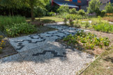 <center>Paray le Monial </center>Derrière la maison de la mosaïque se découvre un jardin mosaïque. Ici les tesselles sont remplacées par des carrés de terre plantés de diverses essences.
Un cheminement en calades complète merveilleusement cet espace. Ce sont des galets posés verticalement sur un lit de sable et de chaux.