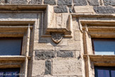 <center>Vias</center>Entre les deux fenêtres, l'écusson est orné de lettres en caractères gothiques. Il s'agit du blason d'un marchand, probablement le propriétaire de la demeure.