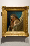 Chut ou Le secret ou Jeune femme. PIERRE-AUGUSTE COT. Huile sur toile, 1869.
Issu d'une famille modeste et né à Bédarieux, petite ville industrielle éloignée de tout centre artistique et proche de Lodève, Pierre-Auguste Cot vient à la peinture grâce à la reconnaissance de son talent par son professeur. En 1860, un tableau à sujet historique, Nysus et Euryale, lui permet d'accéder à l'École Nationale des Beaux-Arts de Paris en même temps que son ami le peintre Jean-Paul Laurens. Cot entre alors dans les ateliers de Cabanel (1823-1889) et de Bouguereau (1825-1905).
Accusé par certaines critiques de « courir après l'effet pittoresque ou après cette espèce d'idéal bourgeois qu'on appelle « l'air distingué », le peintre échappe avec ce portrait précoce, à la peinture académique parfois trop convenue. Une jeune femme en buste et au regard malicieux pose, son corps nu enveloppé dans un drap de soie blanc aux rayures bordées d'un filet rouge. Ses lèvres sont entrouvertes et ses cheveux détachés. De sa main gauche, elle cache son sein en s'enveloppant dans le drap tandis que sa main droite, index pointé devant sa bouche esquisse un geste comme pour supplier le spectateur complice de ne pas la trahir. A-t-elle été surprise dans une posture équivoque ? Que souhaite-elle taire ?