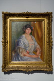 Portrait de Mme Thurneyssen. PIERRE-AUGUSTE RENOIR (1841-1919). Huile sur toile, 1908. 
C'est en 1908 que Renoir fait la connaissance des Thurneyssen. Cette toile est la première d'une longue série de portraits de cette famille que des liens d'amitié croissants unissent au peintre. Monsieur Thurneyssen était un intellectuel de Munich, qui avait hérité d'une entreprise familiale de chimie. Bon client d'Ambroise Vollard et d'autres marchands, il devint en quelques années un des plus grands collectionneurs de Renoir.
Le Portait de Madame Thurneyssen reste fidèle à la peinture de Renoir en poursuivant son hommage à la féminité et à la maternité qui traverse toute son œuvre. Le sujet aux formes généreuses expose sa gorge au spectateur et est vêtu d'une robe diaphane ; la carnation de sa peau rosie ressort en contrepoint sur le bleu froid de la robe. La retenue est bien là, dans le croisement des doigts et l'attitude sage du modèle. Cet équilibre, ou cette tension, se retrouve dans la palette de couleurs de l'arrière-plan, entre jaune-orange fiévreux et vert d'eau, en passant par le triangle de bleu ciel que forme la robe au centre.