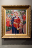 Madone au Jardin fleuri. MAURICE DENIS. Huile sur toile, 1907
Dans la Madone au Jardin fleuri, les personnages centraus sont les mêmes que dans Le bain, mais transfigurés. Marthe serre contre elle sa petite Madeleine (dite Malon), et elle devient une icône de l'amour maternel, évoquant une Vierge à l'Enfant Le peintre respecte les détails matériels, les portraits sont exacts, les vêtements contemporains, avec le petit chignon ou le voile brodé de fleurs pâles, ou encore le tracé des allées du jardin. On reconnaît les sœurs aînées (Noëlle, Bernadette, Anne-Marie) qui jouent dans le jardin, en silhouettes multipliées. Mais elles arrêtent leur farandole devant l'immense tendresse de la scène, devenue symboliquement sacrée ; leur attention se change en prière, et on pourrait les croire devenues des anges. Pour Denis, pas de séparation entre le sacré et le profane, les deux sont intimement mêlés dans la réalité de la vie.
La scène prend place dans le jardin fleuri de Silencio, magnifique villa surplombant la baie de Trestrignel à Perros-Guirec (Côtes d'Armor), louée durant l'été 1906 par les Genêt, amis proches des Denis ; le peintre en fera l'acquisition en 1908.