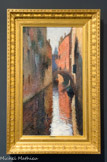 Canal à Venise. HENRI MARTIN (1860-1943). Huile sur toile, ca.1910
Les zones de contacts entre terre et eau furent des lieux élus par Henri Martin pour leurs possibilités picturales. Une touche dissociée très libre pouvait en effet s'y exercer avec bonheur. Après Marseille et avant Collioure où il achète une maison en 1923, Venise fut un de ses séjours de prédilection dès les années 1900. Aux palais somptueux, aux monuments insignes et aux vastes perspectives du grand canal et de la lagune, il préféra souvent les vues plus intimes des petits canaux.
Ici le format vertical et la perspective accentuent l'impression d'étroitesse d'un rio enserré entre de hauts murs. L'apparente facilité de la composition, restituant l'illusion d'une réalité vécue par le spectateur, cache en fait un formidable savoir-faire. Un point de fuite central organise en effet le tableau autour des grandes lignes de fuite obliques de l'architecture des palais ; elles mènent l'œil vers la silhouette gris bleu d'un campanile à l'arrière-plan. Les verticales majeures des arrêtes de briques et de leurs reflets, les pans géométriques des murs rose orangé et ocre jaune, en lumière et très vifs à droite, dans l'ombre, assourdis de bruns et de gris, à gauche, s'agencent en un puzzle de couleurs.