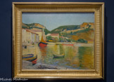 Le Port de Cassis. CHARLES CAMOIN. Huile sur toile, 1901.
Le Port de Cassis, dont le premier propriétaire était le Docteur Reynolds qui avait soigné Van Gogh en 18E9 et reçu en dédommagement son portrait par l'artiste (Portrait du Dr Rey, Musée Pouchkine, Moscou), fut très probablement peint en 1901. Particulièrement lumineux, le tableau témoigne de la bonne connaissance qu'a déjà alors Camoin de la peinture impressionniste. La couleur est appliquée par petites touches dont la taille et les accents varient selon les éléments : la surface de l’eau est ainsi animée d'un entremêlement de touches jaunes, vertes, bleues et orangées alors que le ciel est composé de légers frottis d'un bleu lavé. L’accord orange/vert domine l'ensemble et restitue la clarté du port qui apparaît comme un gemme scintillant inscrit dans son écrin de montagnes. Le caractère très construit de la composition, qui s'articule à partir du dessin précis des quais et des bateaux, confère toutefois au tableau un aspect très classique dans sa facture.