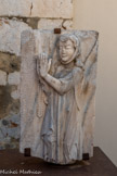 <center>Le couvent des franciscains.</center>Priante, marbre de Céret blanc veiné de bleu. Cette grande plaque est amputée de toute sa partie inférieure. La partie conservée représente la sculpture en ronde-bosse d’une femme debout, de profil, les clos, les mains jointes tenant un chapelet. Elle est vêtue d’une longue robe drapée sous une vaste cape. Un fermoir noue deux cordons décorés par deux pompons pour retenir la cape sur les épaules à lae hauteur de la poitrine. Cette image figure une « priante » et s’oppose ainsi à la représentation antérieure du « gisant ». Elle évoque l’évolution des mentalités médiévales face à la mort. L’horizontalité du gisant signale un cadavre alors que la verticalité du priant indique la vie éternelle. De même les mains jointes du « priant » lui donna son nom à la différence du « orant » qui a les mains levées et ouverte du côté des paumes.