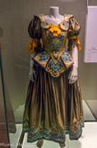 <center></center><center>Couloir de la mode.</center> Robe en taffetas de soie bronze, avec application de soie et sequins. Ballet Le Chat Botté, création 1995, Paris. Première dansée à Paris, puis en janvier 1996 à Marseille. Chorégraphie, Roland Petit. Décors, Josef Svoboda. Costumes, Franca Squarciapino.