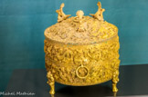 <center>Le jade</center>Récipient de type Zun pour les libations.
(Dynastie des Han de l’Est, 25-220)
0r, incrustations de turquoise
Ce récipient de type zun est destiné à recevoir les boissons fermentées, alcoolisées, lors des cérémonies rituelles ou bien lors des banquets La pièce comprend un couvercle amovible sur lequel trois motifs propitiatoires (porte-bonheur) de phénix, retiennent l’attention.
Sur le pourtour, des dragons sans cornes, de type panchi, tout en sinuosités, donnent une dynamique particulière à l’ensemble. Trois anneaux sont présenta à mi-hauteur, tandis que trois pieds de bêtes féroces soutiennent l’ensemble. Sous la base, des caractères indiquent l’année de réalisation ( pièce) durant la vingt quatrième année de l’ère Jiangwu, c’est -à dire e sous le règne de l’empereur Guangwu, au pouvoir de 25 à 57.