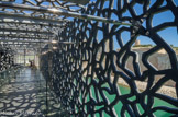 <center>Le déambulatoire du MuCEM.</center> Cette dentelle de béton fibré ne joue aucun rôle structurel. Elle sert de filtre en protégeant le cube intérieur du Mucem et la promenade périphérique du soleil et du vent. Son motif peut évoquer de multiples références comme le moucharabieh ou la structure du corail.