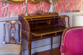 La chambre de Pauline de Caumont.<br>Ce bureau à cylindre est typique du style Louis XVI : ses pieds droits, son placage et ses bronzes aux motifs antiquisants sont autant de caractéristiques. Rompant avec les excès rocaille, les lignes se font droites et sobres, de même du placage de ho s uni. Introduit en France sous le règne de Louis XV, ce type de meuble permet de cacher sa correspondance des regards indiscrets en fermant le volet. Le plus célèbre bureau a cylindre reste celui commandé en 1760 par Louis XV à l'artisan Jean-François Oeben et achevé par Jean-Henri Riesener aujourd'hui encore conservé au château de Versailles.