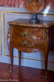 La chambre de Pauline de Caumont.<br>Petite commode au placage de bois précieux. Estampillée Corbet et frappée aux quatre coins des montants d'une fleur de lys, elle réunit toutes les qualités d'un meuble de style Louis XV. Elle repose sur quatre pieds galbés et élancés, est habillée d'un placage de bois précieux disposé en frisage et s'ouvre à deux tiroirs ornés de bronze doré.